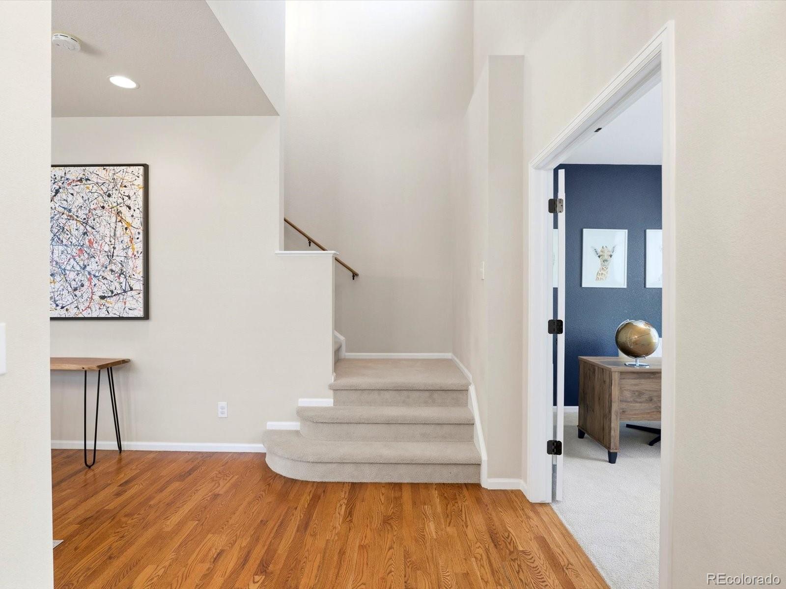 Entry foyer with hardwood floors, a tall ceiling, and a curved carpeted staircase beside a blue-walled room.