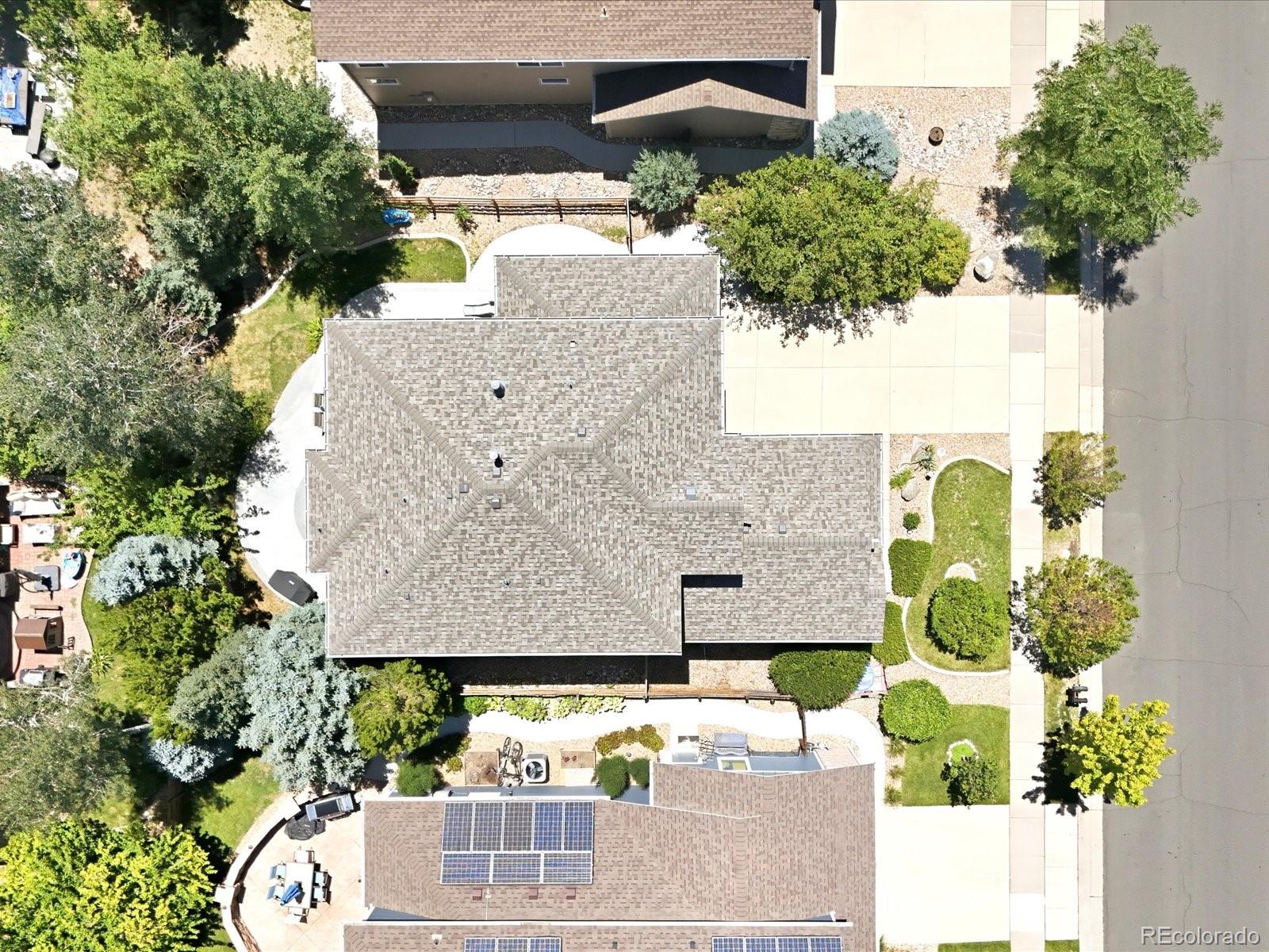 Aerial view of a gray-shingled house surrounded by trees, garden paths, and landscaped lawn.