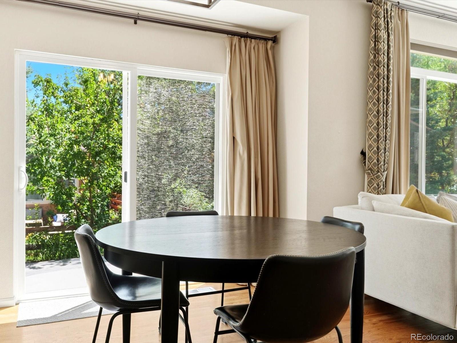 Dining area with a round dark table beside sliding glass doors opening to a leafy patio.