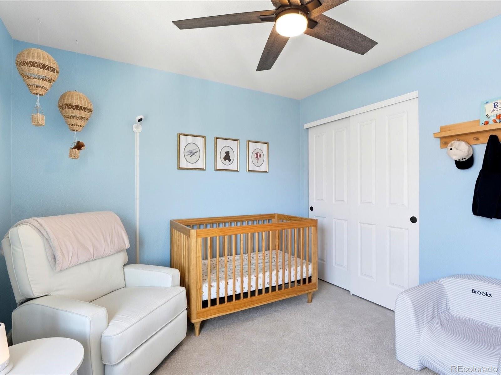 Nursery with a wooden crib, white glider, pale blue walls, and woven hot-air-balloon decorations.