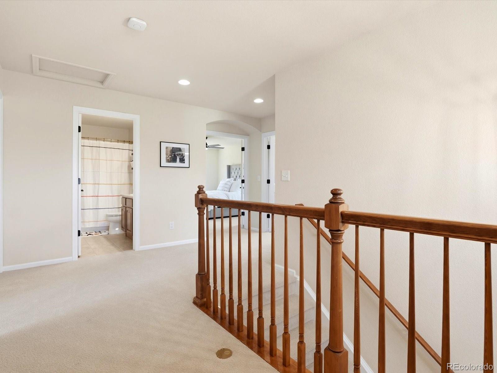 Upstairs landing with cream carpeting, a dark wood stair railing, and open doorways to a bathroom and bedroom.