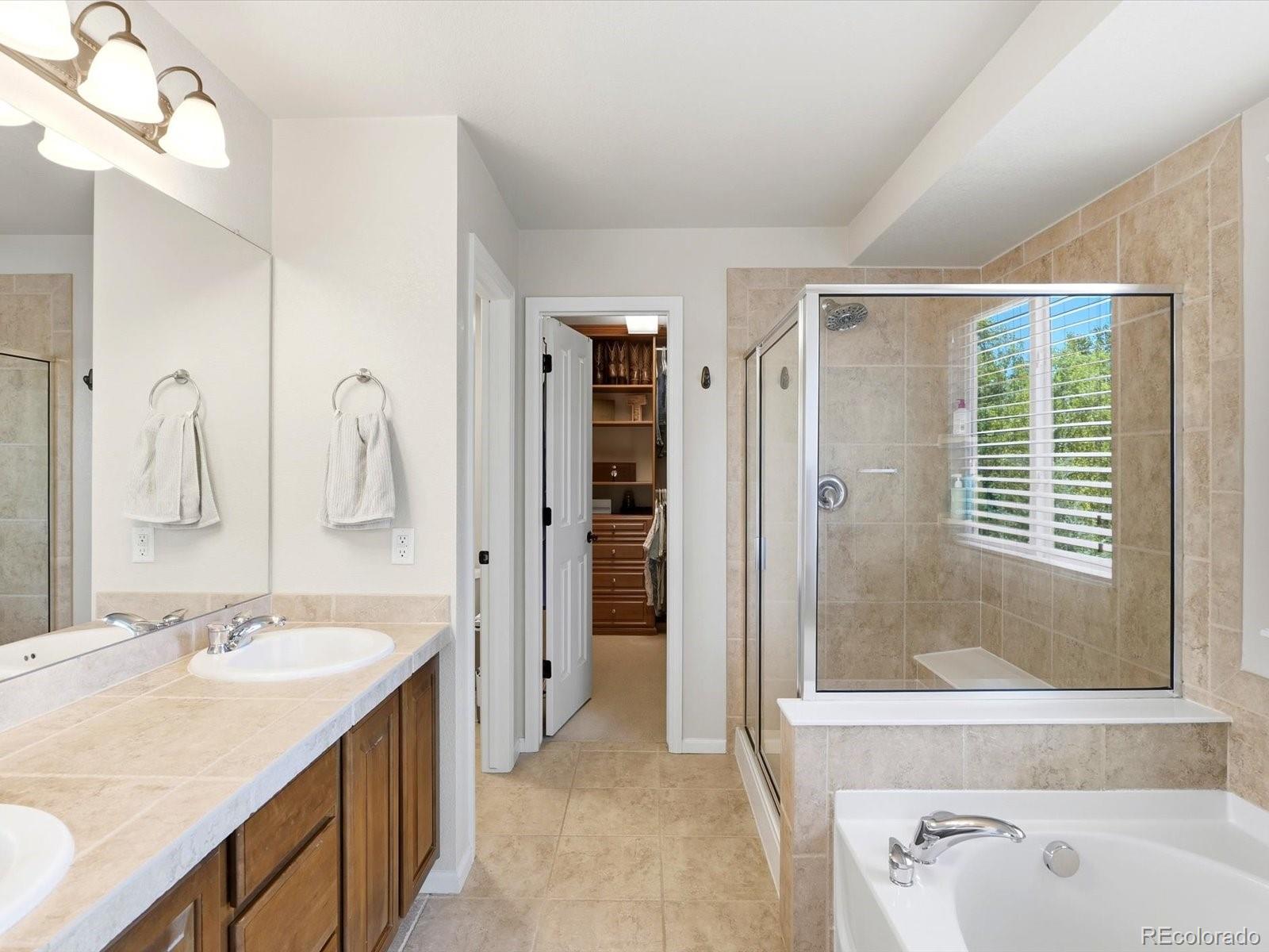 Bathroom with a glass-enclosed tiled shower, soaking tub, and vanity beside an open walk-in closet.