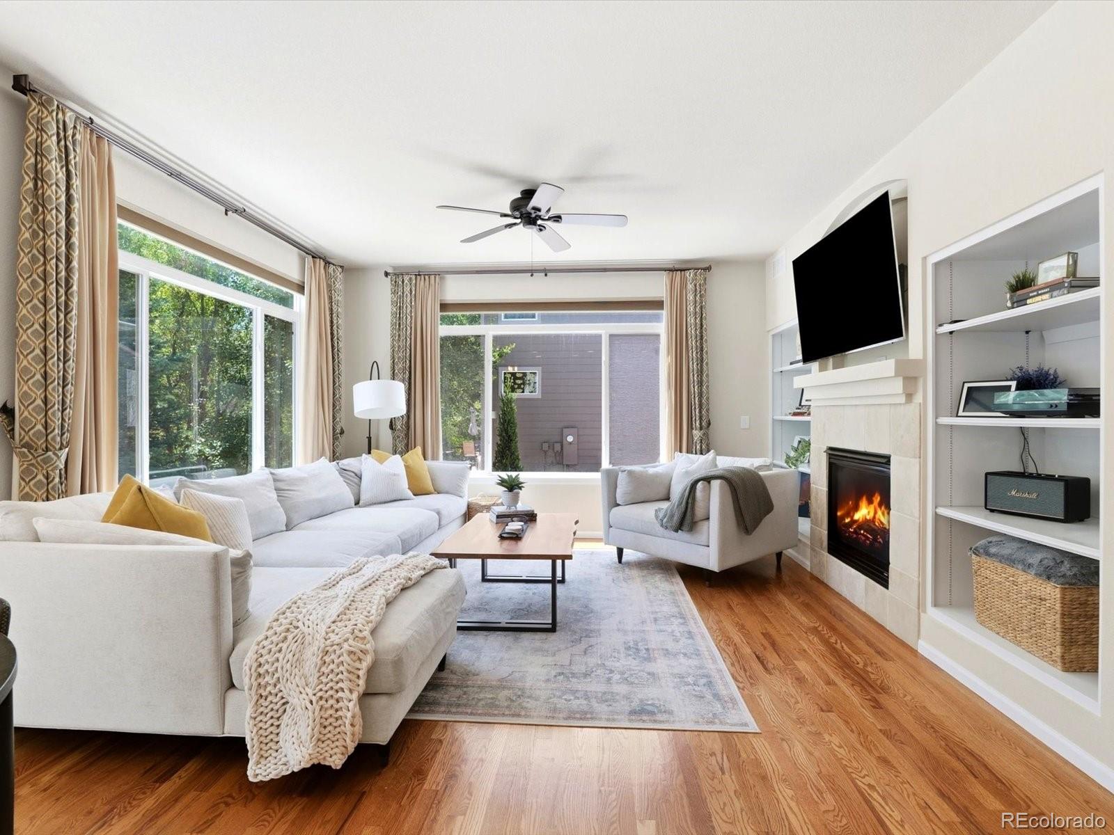 Bright living room with a white sectional, fireplace, built-in shelves, and large windows.