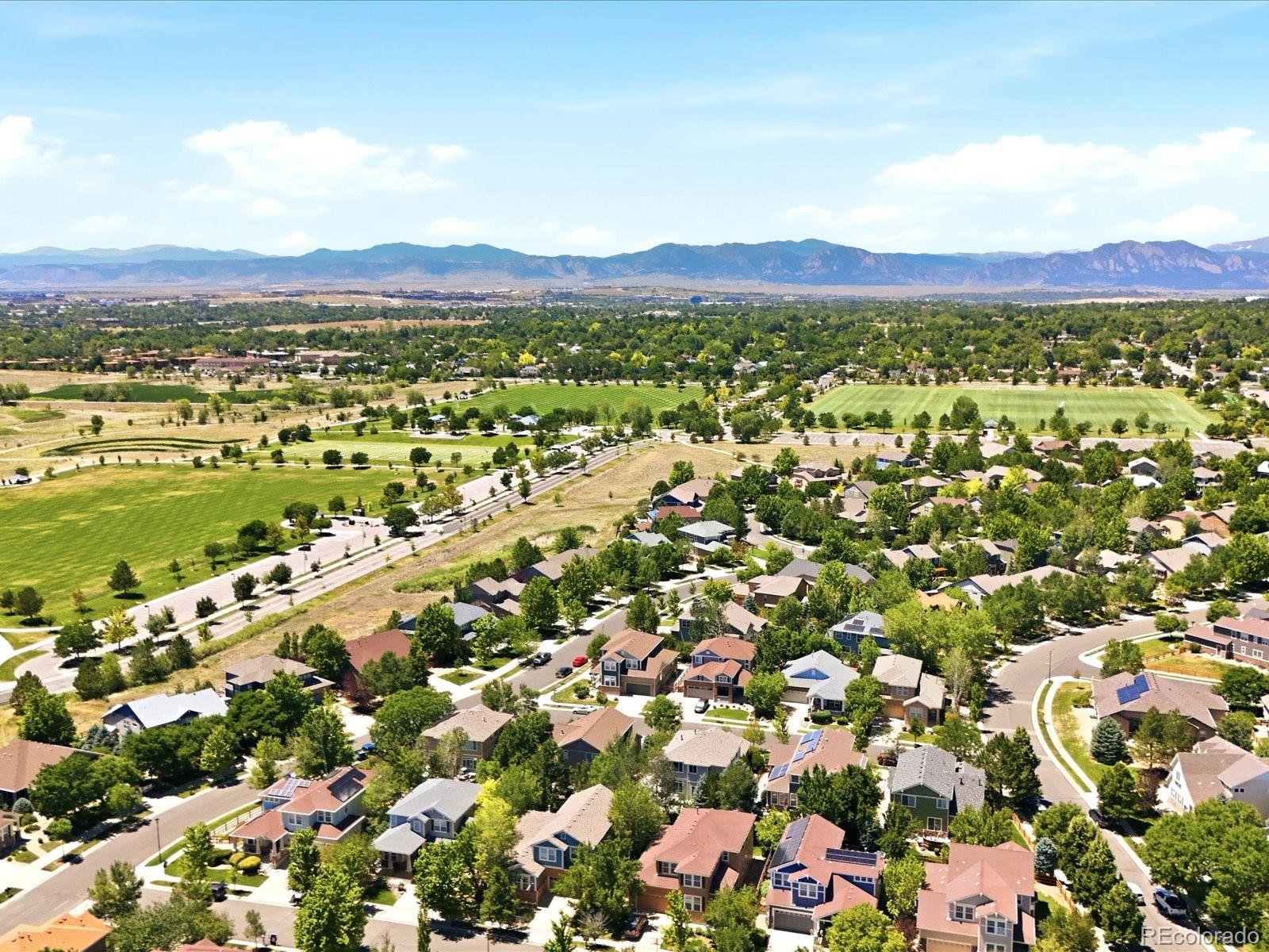 Aerial view of a Broomfield neighborhood, green fields, and the Rocky Mountains.