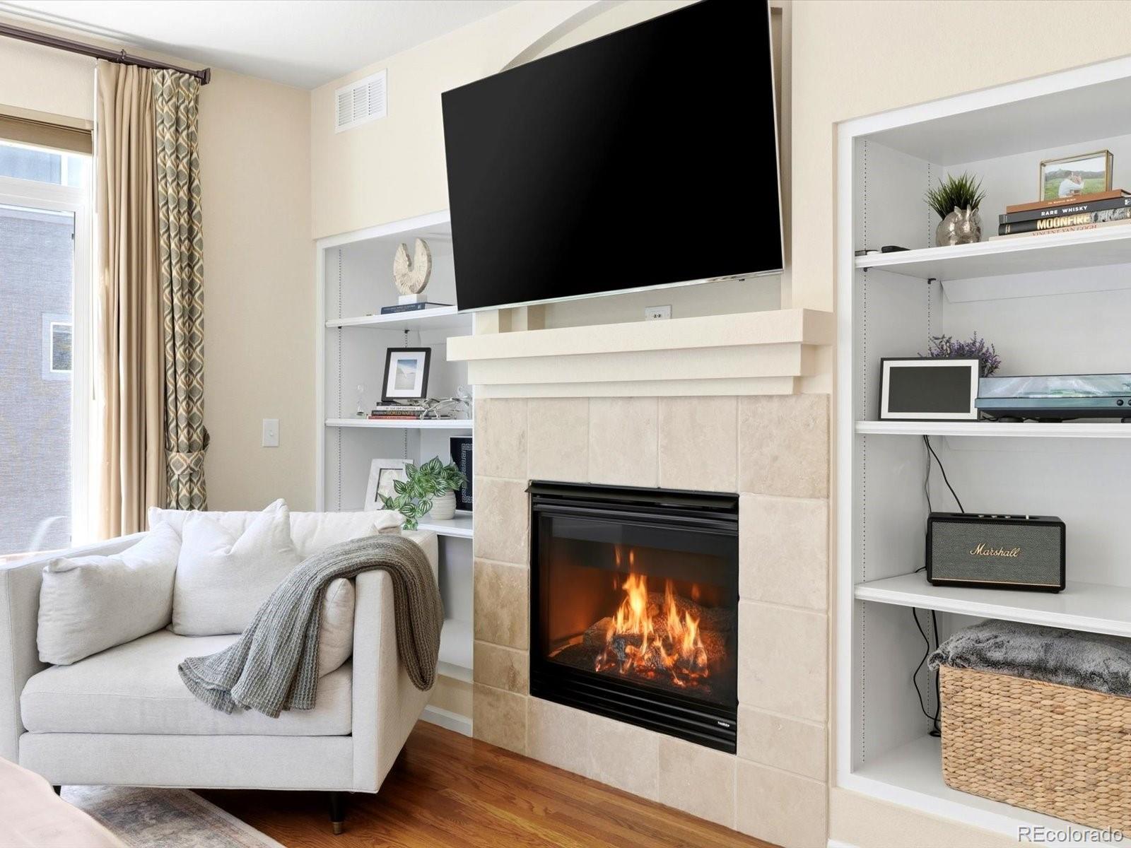 Living room with a cream sectional, tiled fireplace, large television, and white built-in shelves.