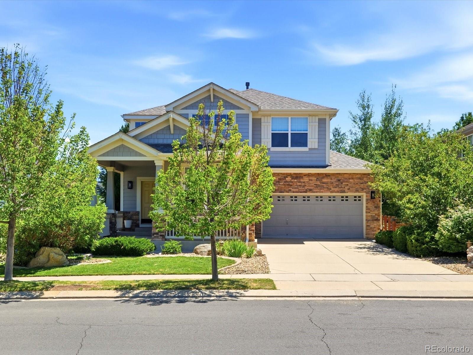 Two-story blue-gray home with stone facade, double garage, and landscaped front yard.