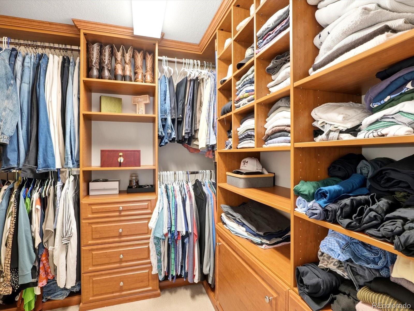 Walk-in closet with extensive wood shelving, hanging clothes, and a central chest of drawers.