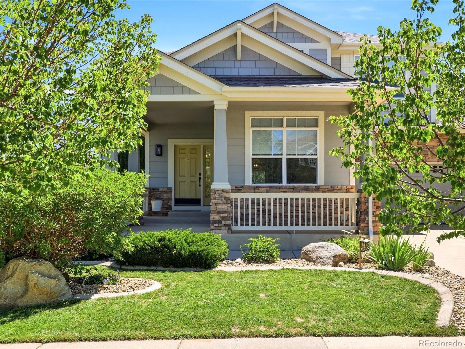 Gray gabled home with a covered porch, stone accents, and a landscaped front lawn.