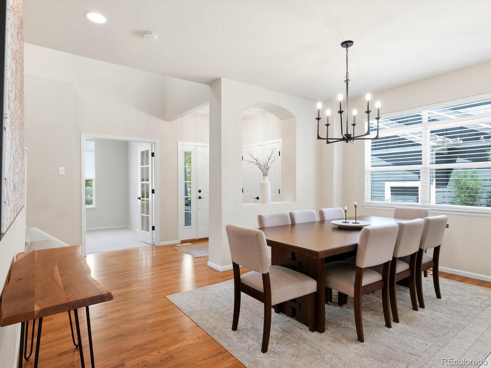 Dining room with a dark wood table, upholstered chairs, and a black chandelier beside large windows.