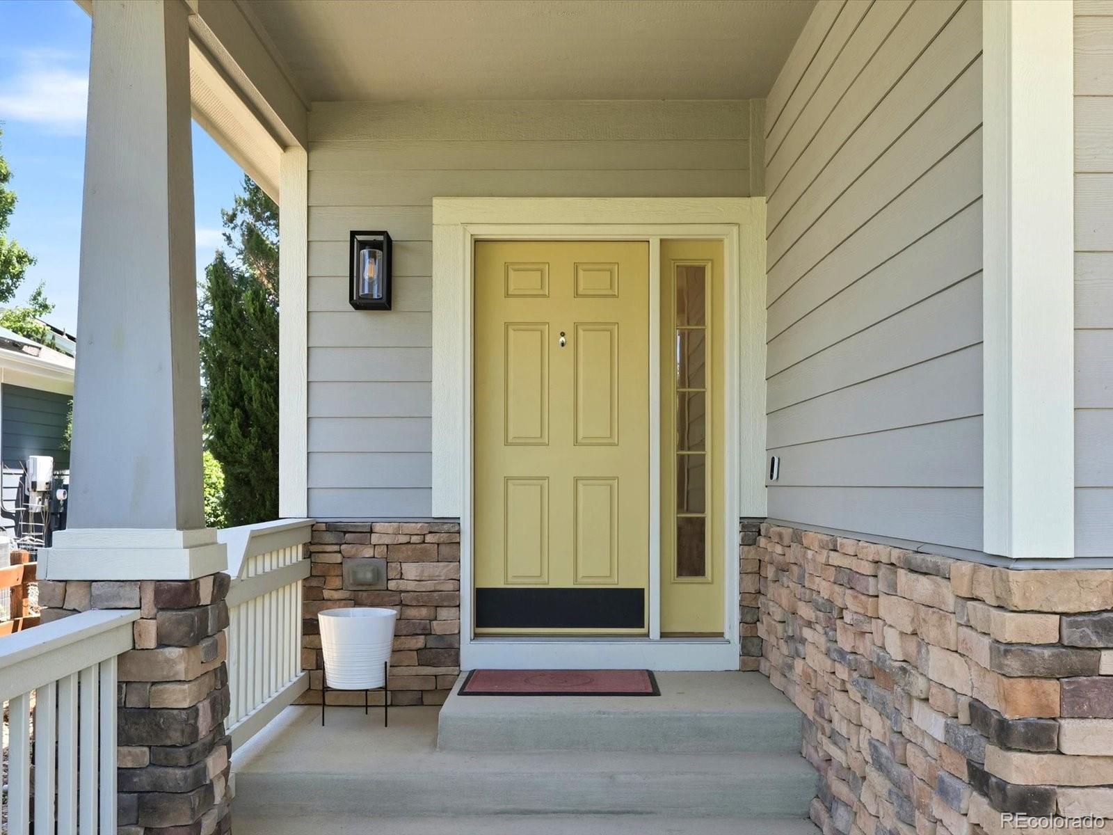 Home’s covered entry with a yellow front door, stone veneer, and white porch railing.