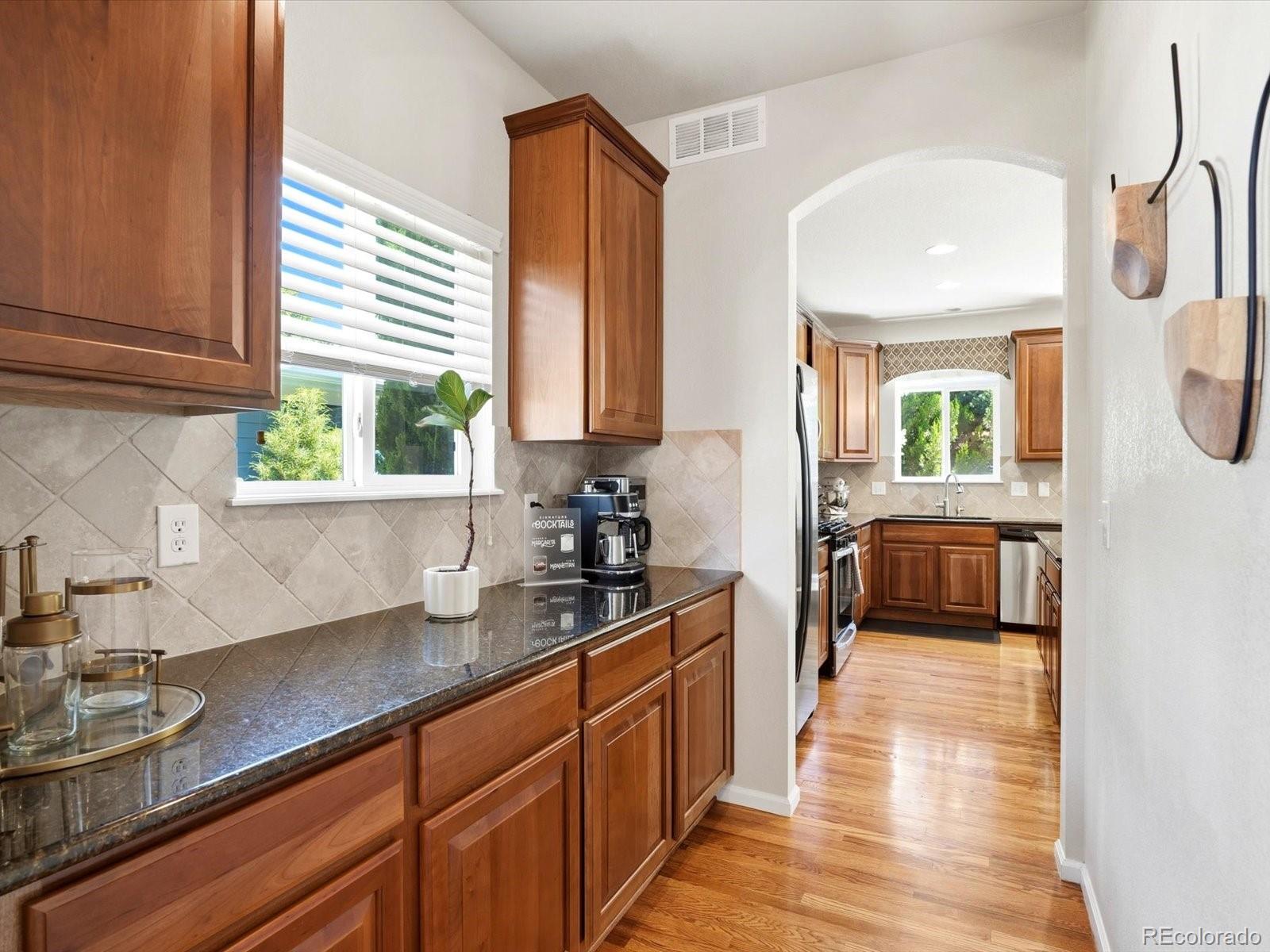 Kitchen with warm wood cabinets and dark countertops, looking through an archway to a second kitchen area.