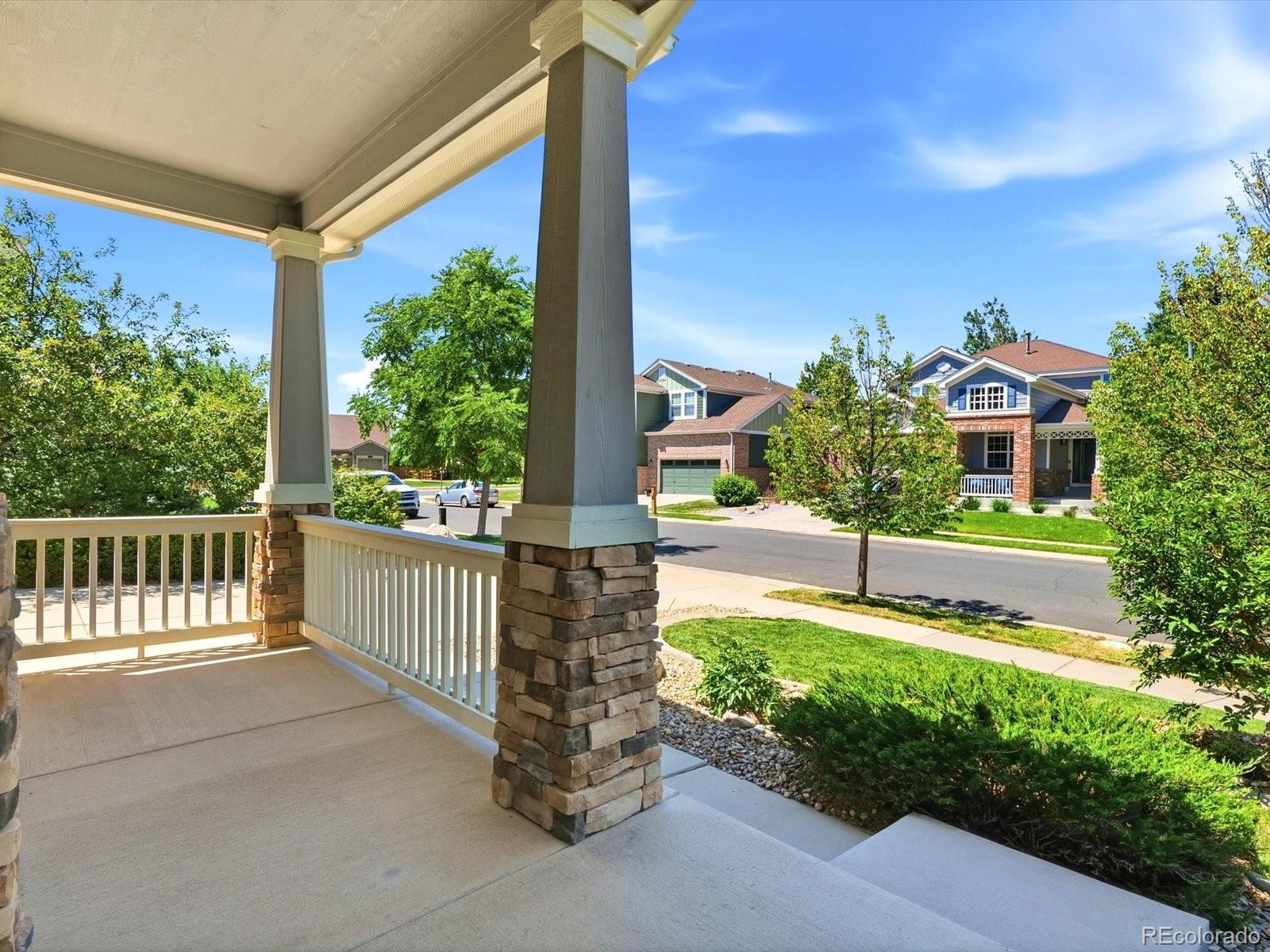 Covered front porch with stone columns and white railings overlooking a tree-lined residential street.