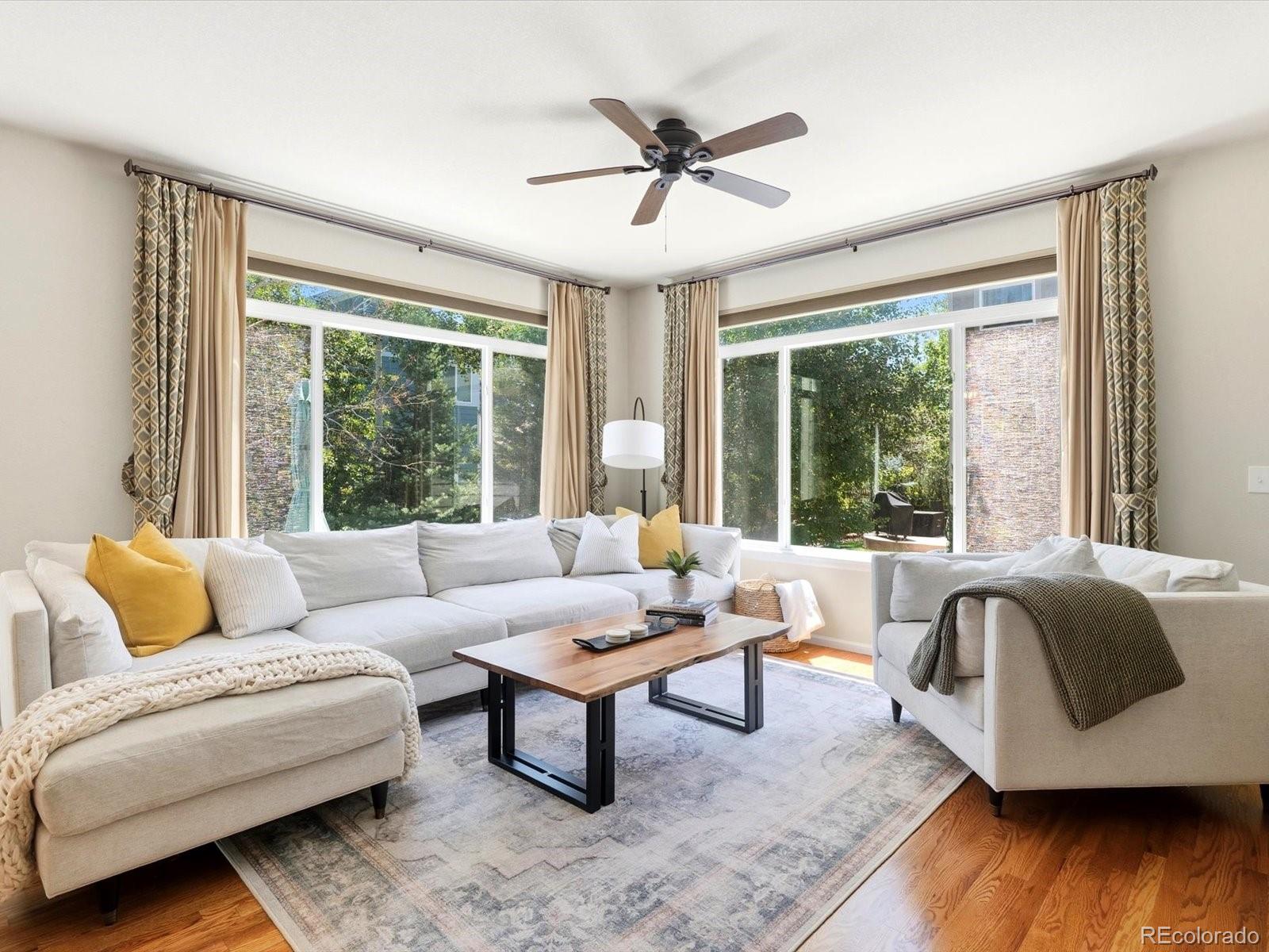 Living room with white sofas, a wood coffee table, and large corner windows overlooking greenery.