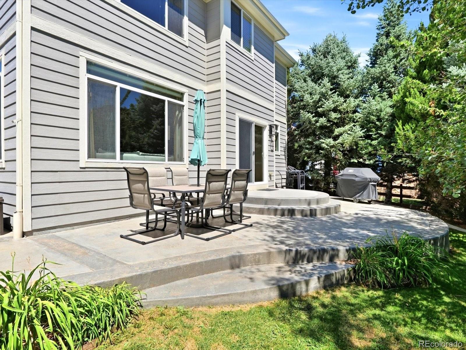 Rear patio with outdoor dining set and umbrella beside the gray-sided home.