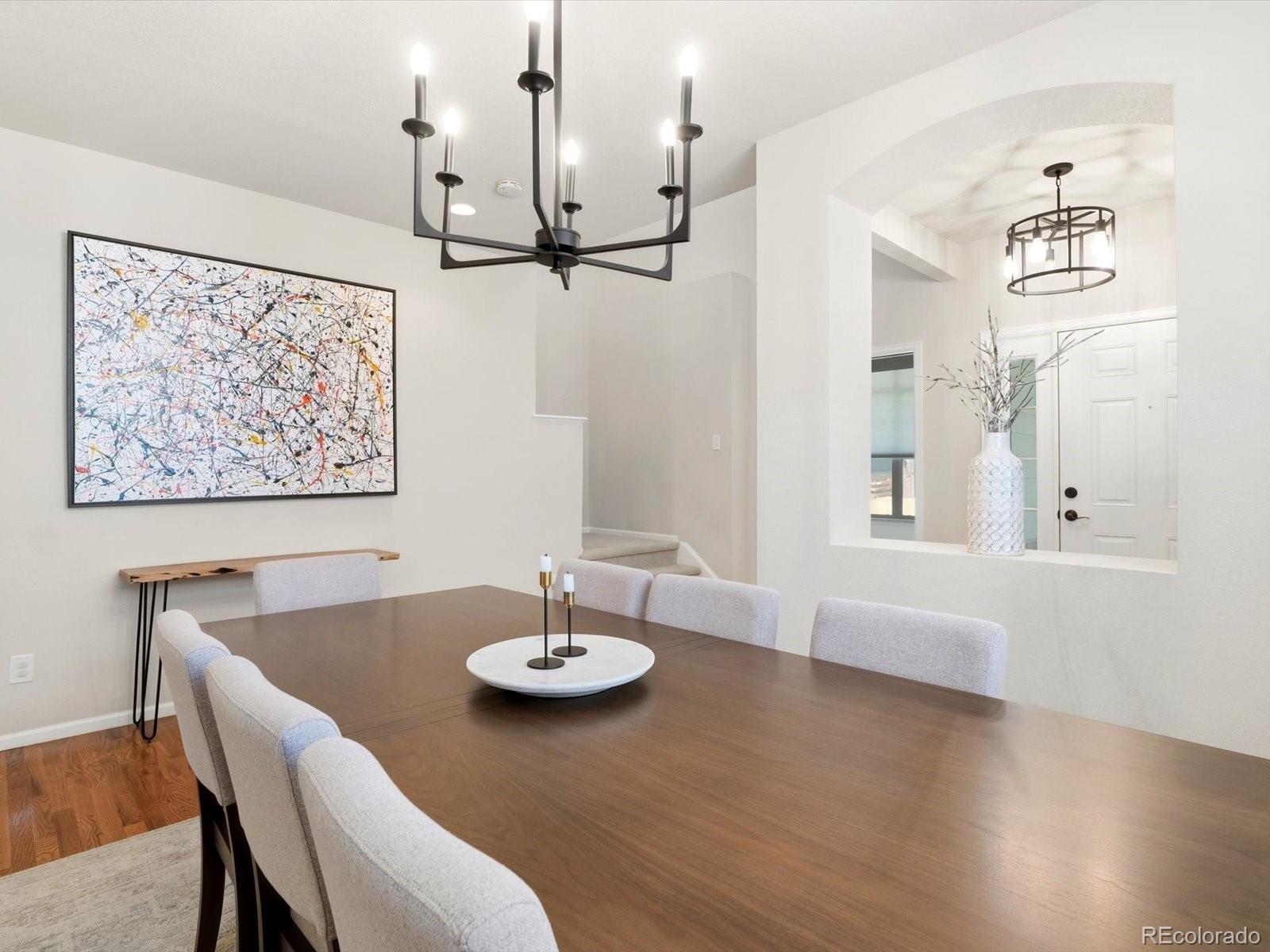 Dining room with a wooden table, upholstered chairs, black chandelier, and arched opening to the entryway.