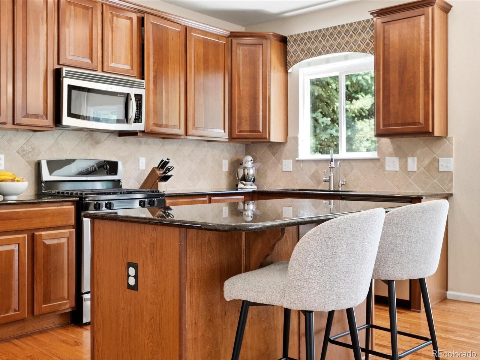 Kitchen with warm wood cabinetry, a dark stone island, and two upholstered bar stools.