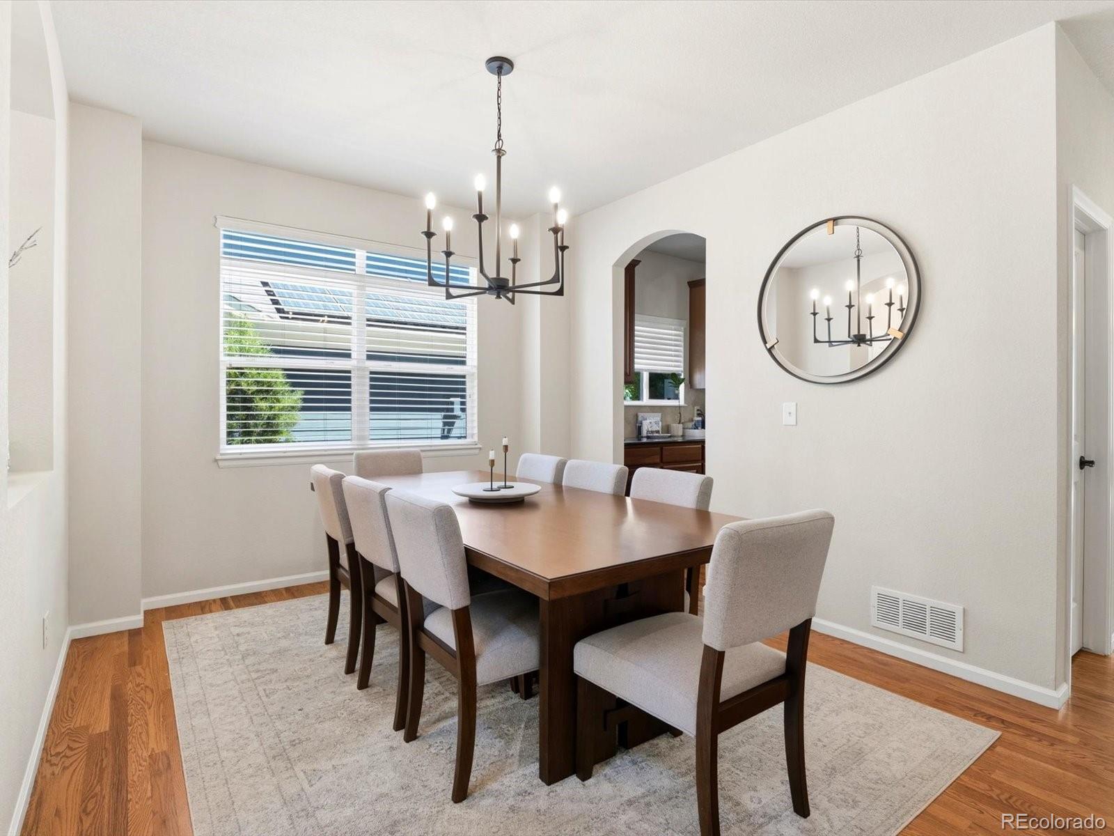 Dining room with a dark wood table, upholstered chairs, black chandelier, and round wall mirror.