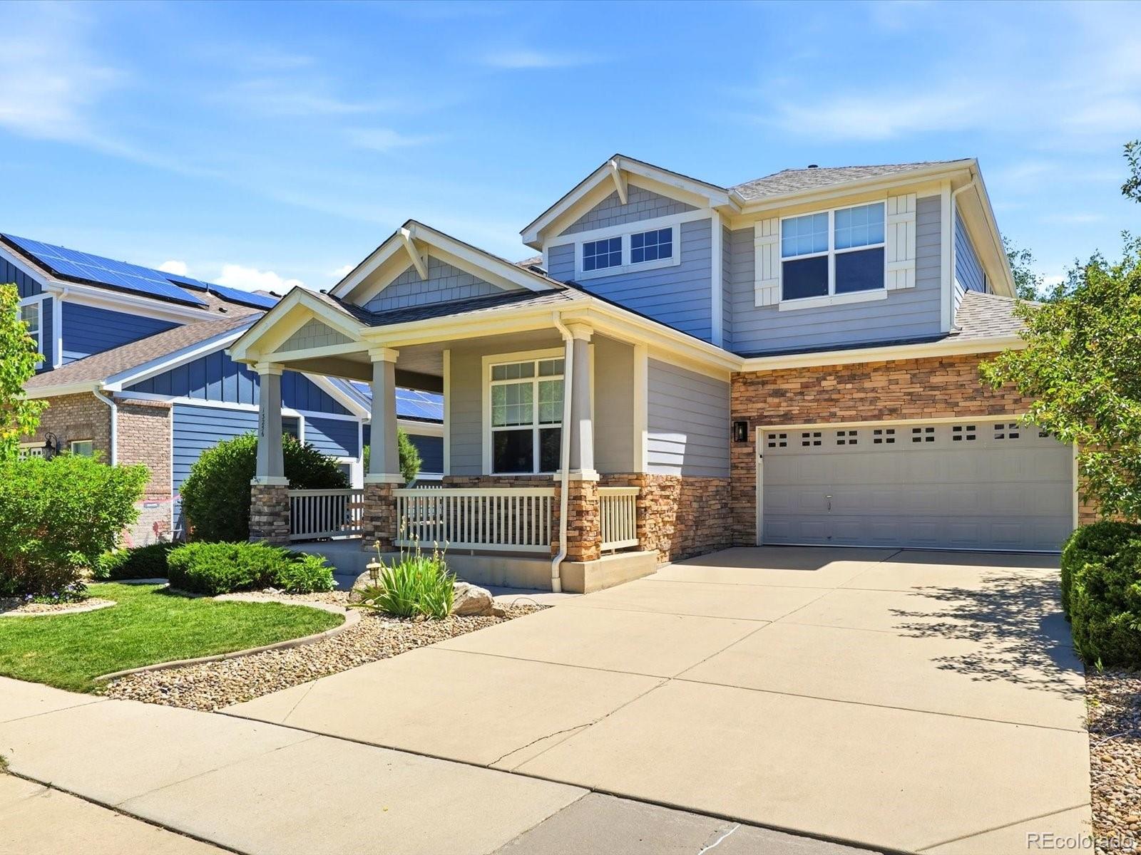 Two-story gray house with a stone-accented porch, attached garage, and landscaped front yard.