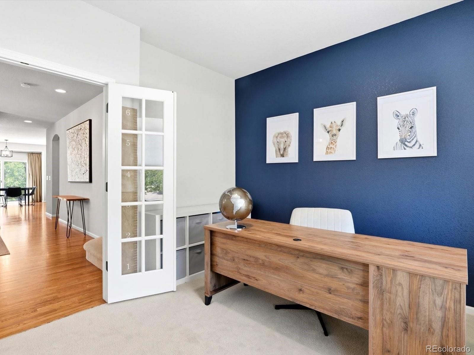 Furnished home office with a wood desk, navy accent wall, and framed animal prints.