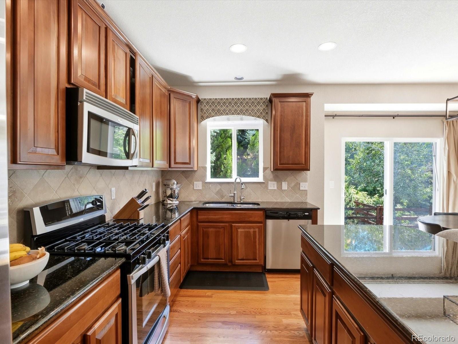 Kitchen with rich wood cabinets, granite counters, a gas range, and windows overlooking greenery.