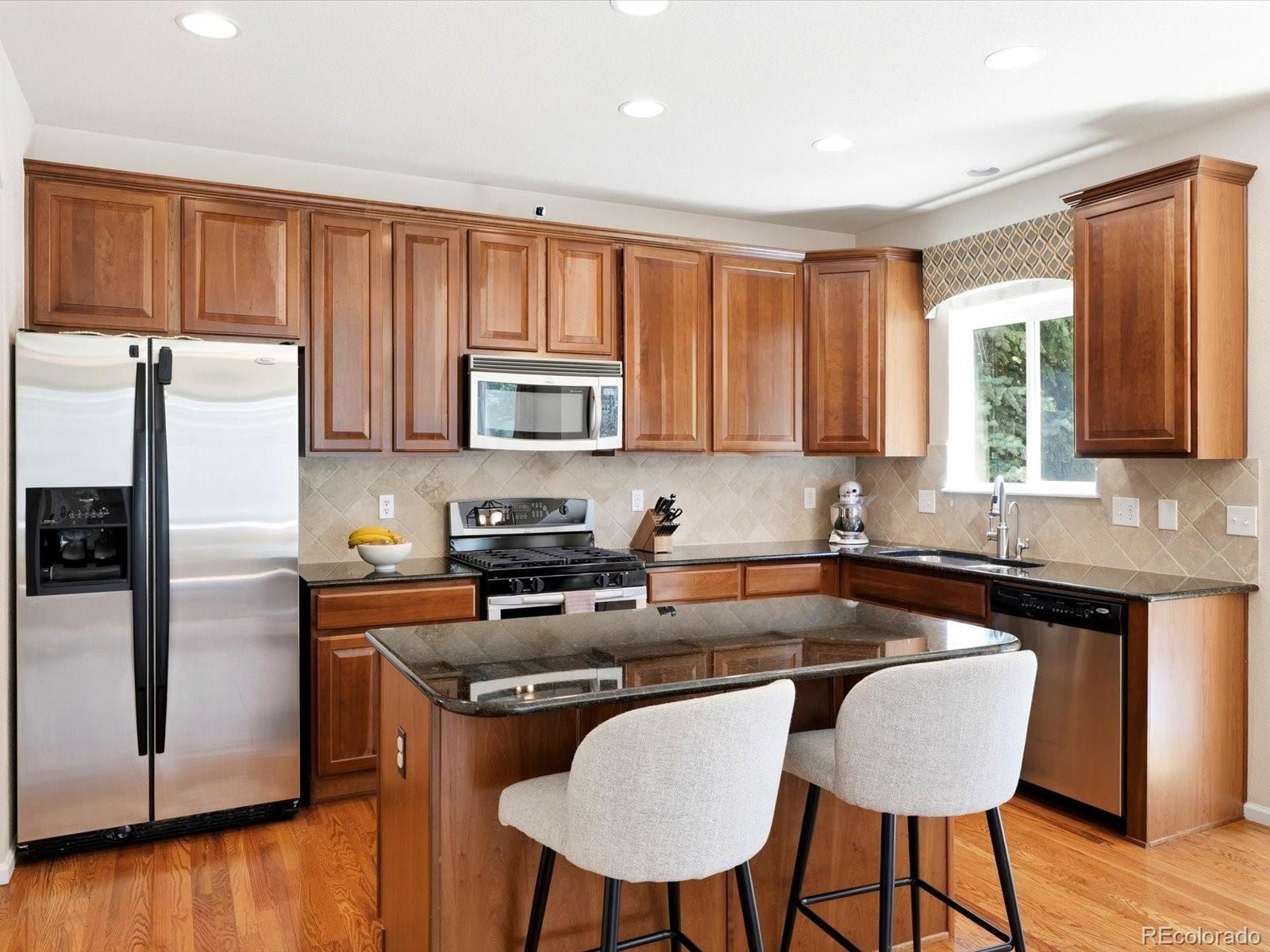 Kitchen with warm wood cabinets, stainless steel appliances, and a central island with two stools.