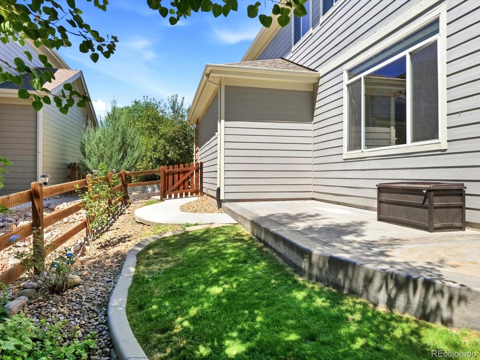 Backyard patio beside a gray-sided home, with a curved lawn, rock landscaping, and wooden fence.