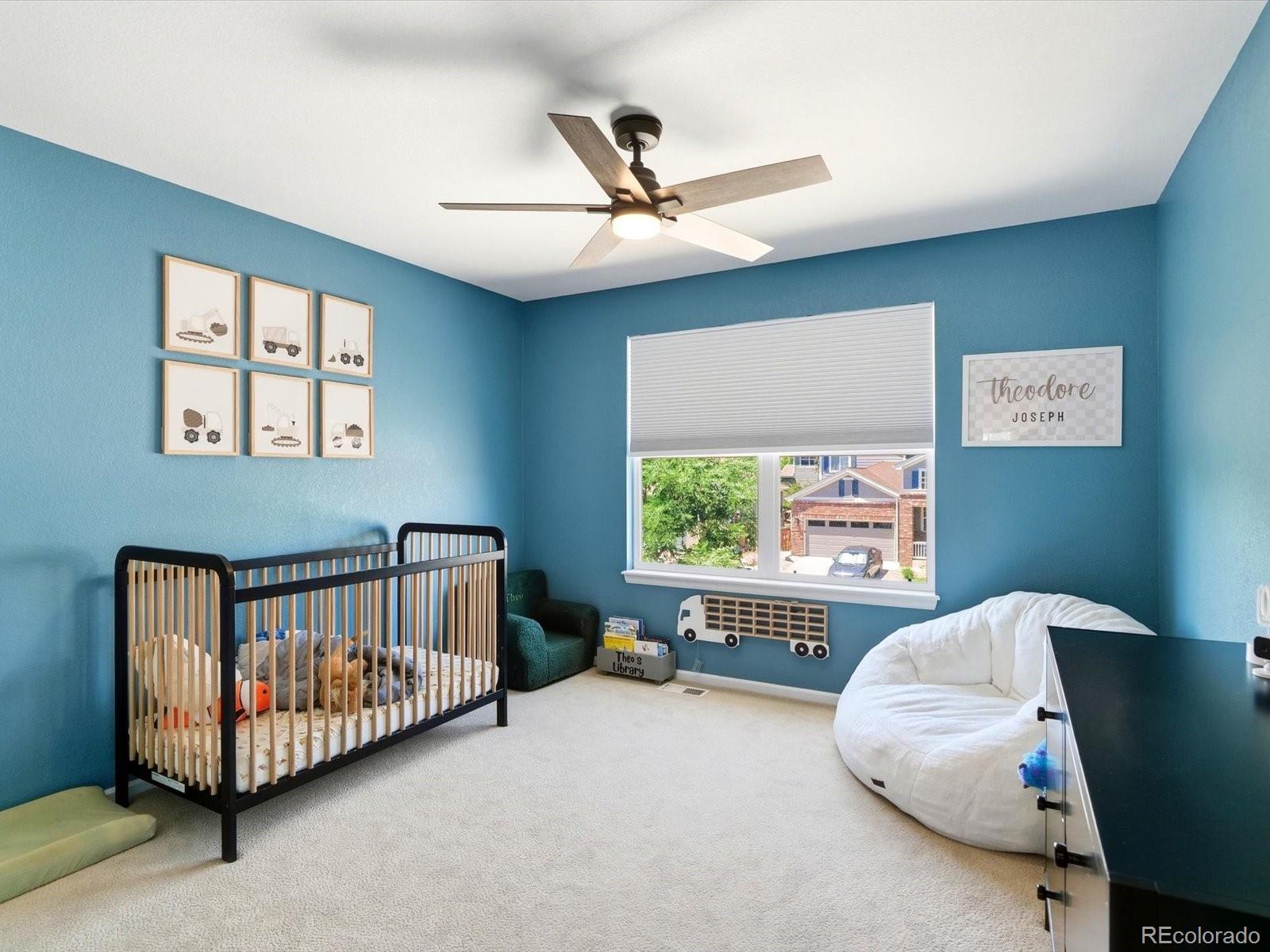 Teal nursery with a black crib, vehicle artwork, and a window overlooking a neighboring house.
