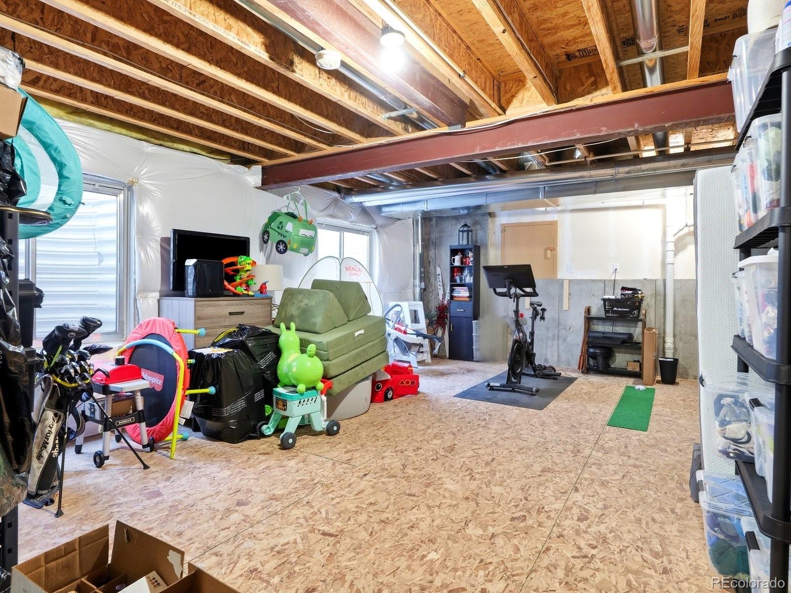 Unfinished garage with exposed joists, storage shelves, children’s toys, and exercise equipment.