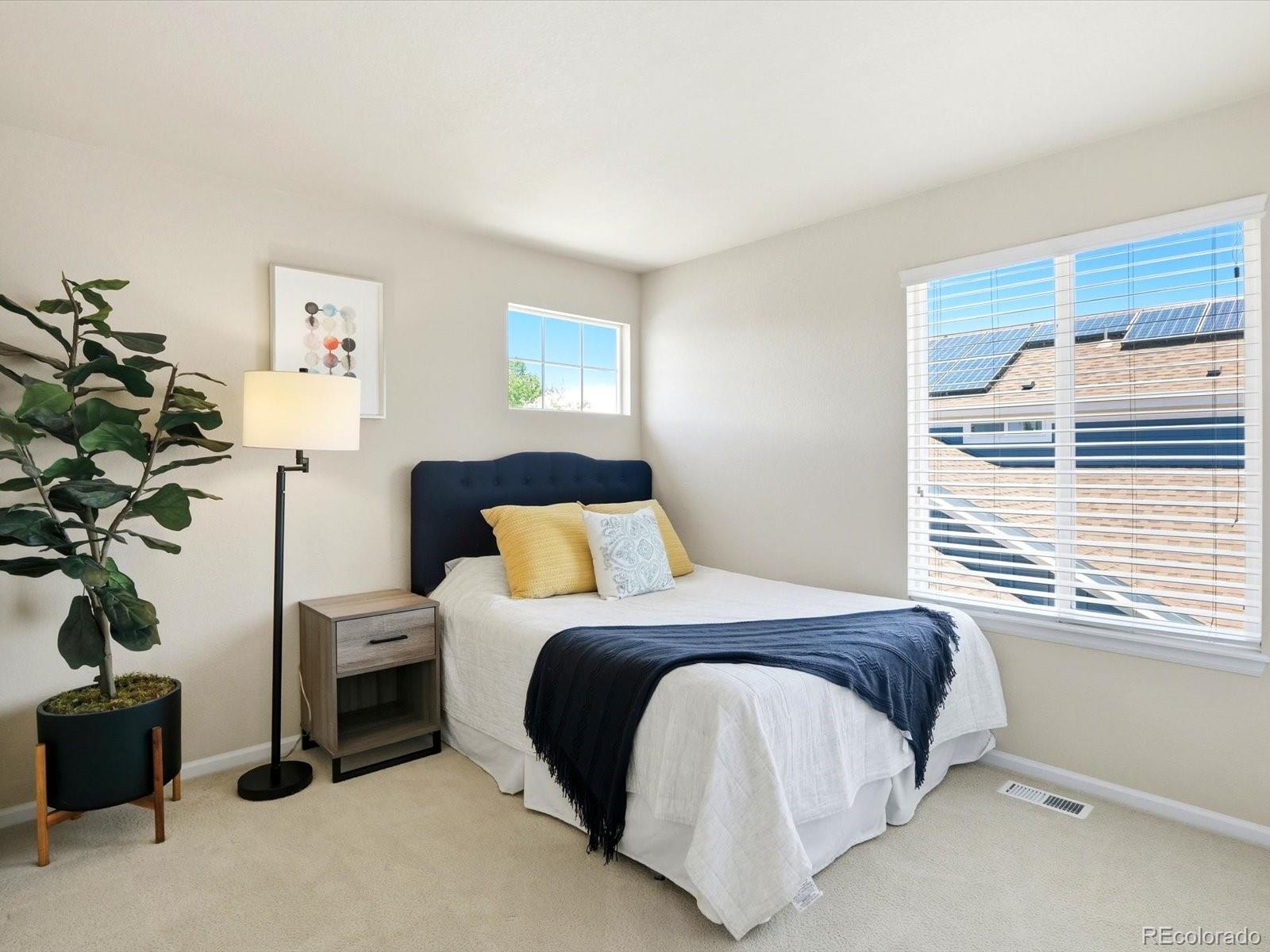 Staged bedroom with a navy upholstered bed, bright windows, and solar panels visible outside.