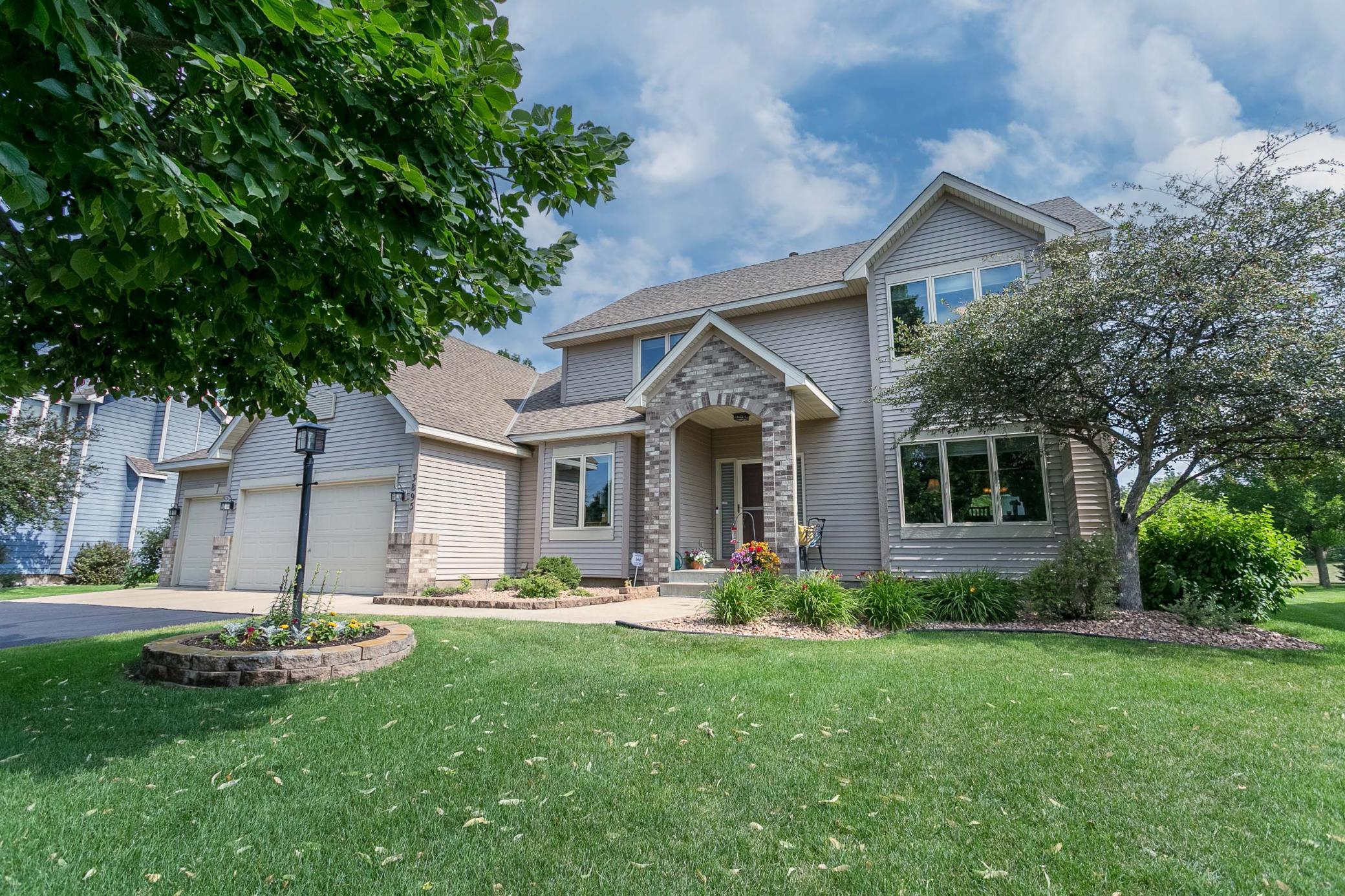 Two-story gray house with a brick arched entry, double garage, flower beds, and broad front lawn.