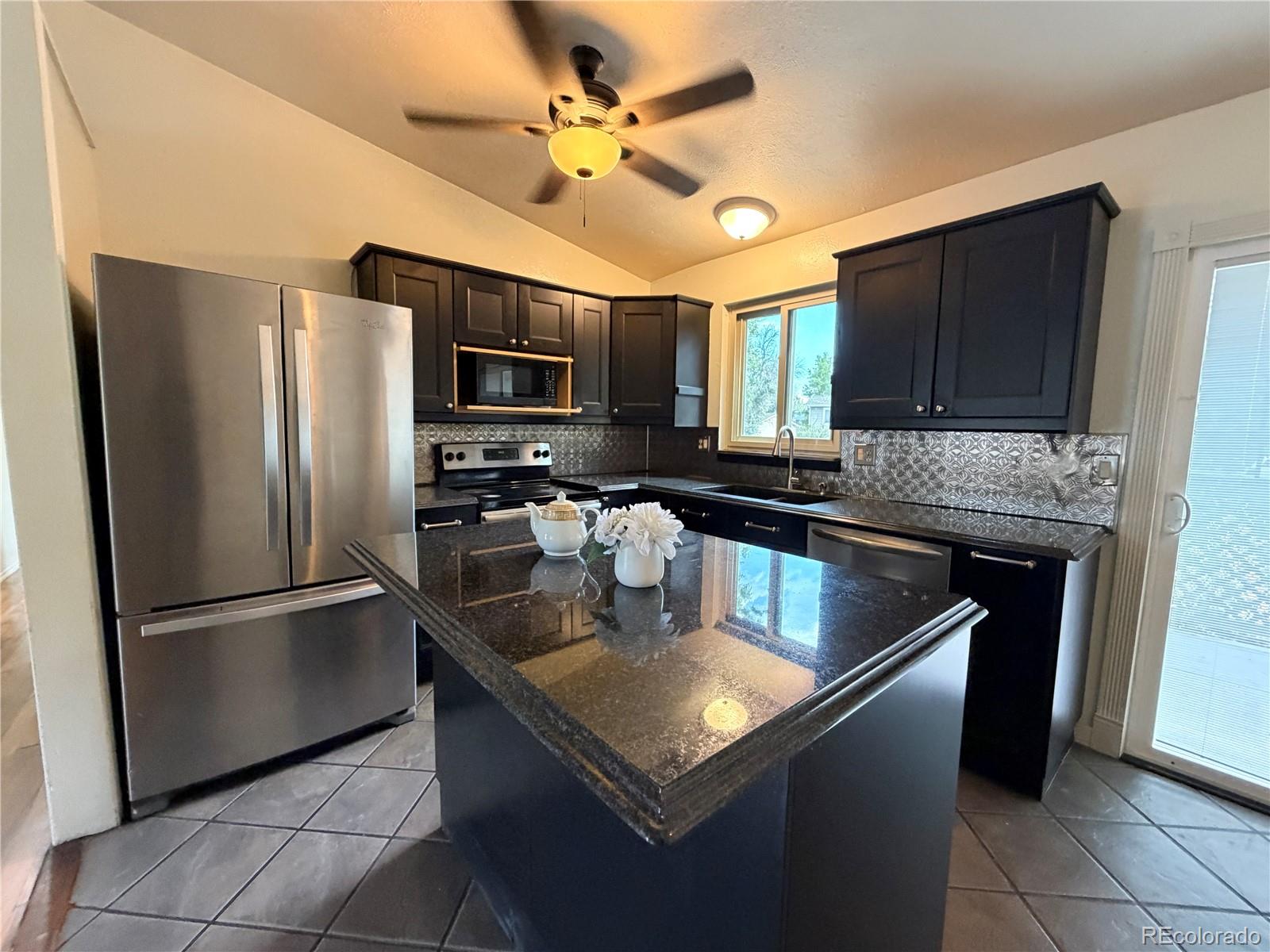 Kitchen with dark cabinets, stainless steel appliances, patterned backsplash, and a large stone island.