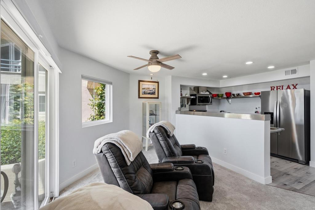 Living room with black reclining chairs, sliding glass doors, and an open kitchen with a white breakfast bar.
