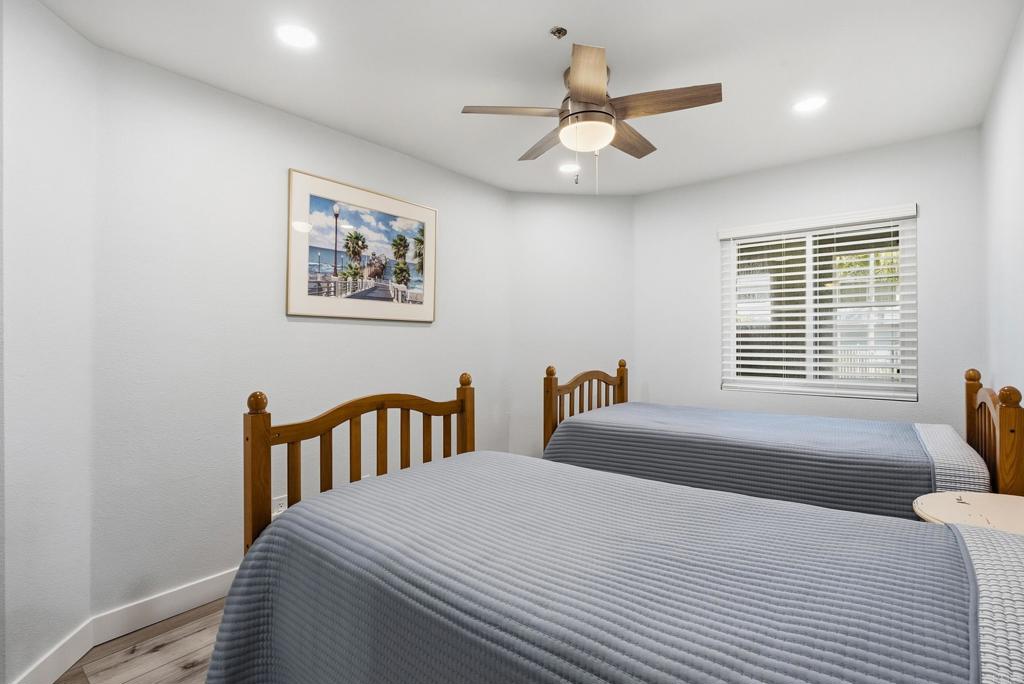 Bedroom with two wooden twin beds, gray bedding, a ceiling fan, and a window with blinds.