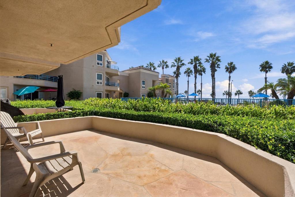 Condo patio with lounge chairs, landscaped planters, palm trees, and a glimpse of the ocean.