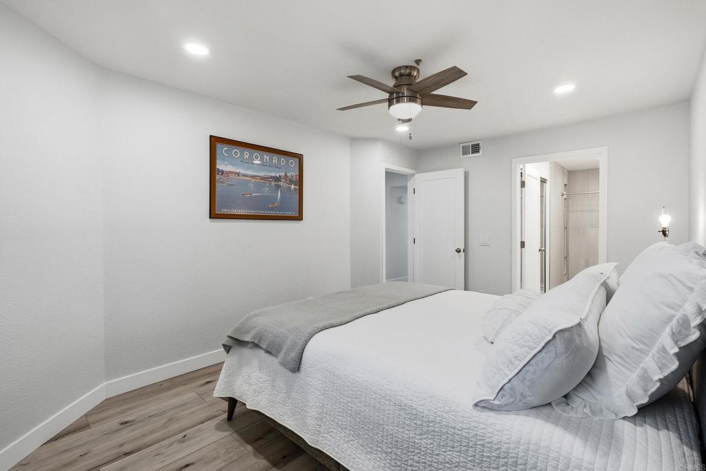Bedroom with a white quilted bed, gray throw, ceiling fan, and framed Coronado print.