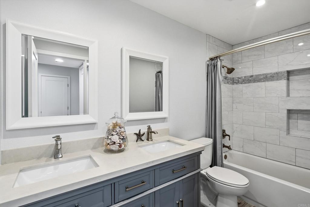 Bathroom with a blue-gray double vanity and a marble-look tiled tub surround.