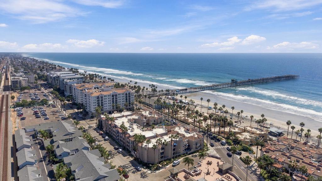 Aerial view of Oceanside beachfront condos, sandy shore, and long pier extending into the Pacific.