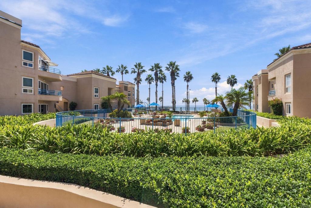 Condominium courtyard with a swimming pool, palm trees, and ocean view between the buildings.