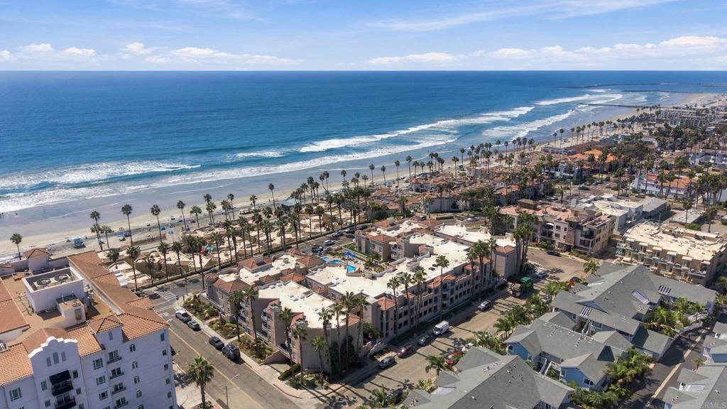 Aerial view of Oceanside beachfront, with Pacific waves, sandy shore, and palm-lined coastal buildings.