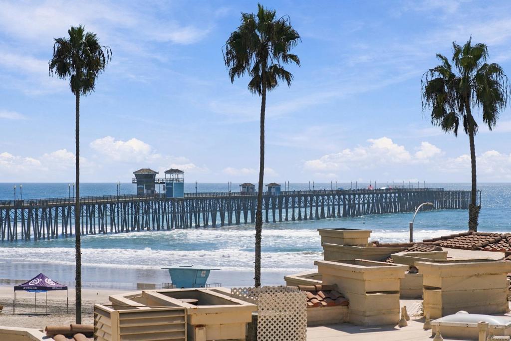 Ocean and Oceanside Pier framed by palm trees, with beachfront rooftops in the foreground.