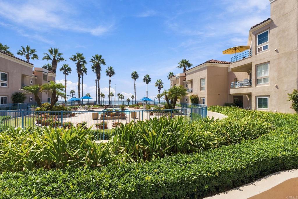 Condominium courtyard with palm trees, blue umbrellas, and an ocean view.