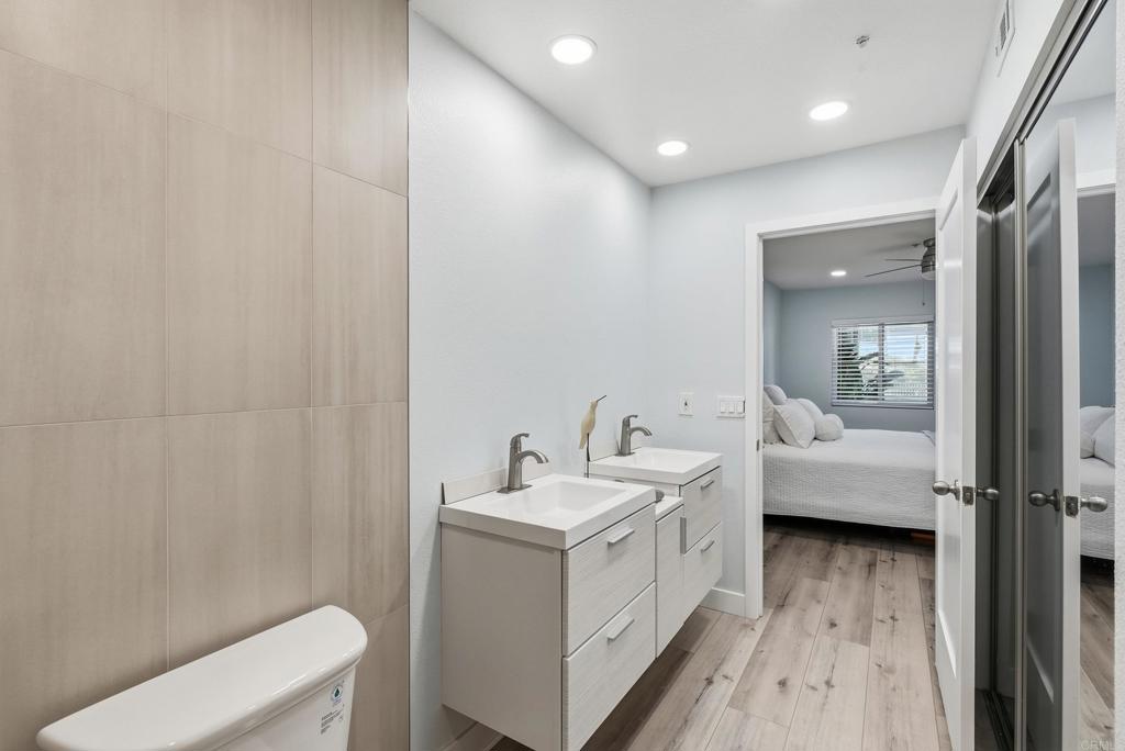 Bathroom with two vanities and wood-look flooring, opening to a bedroom.