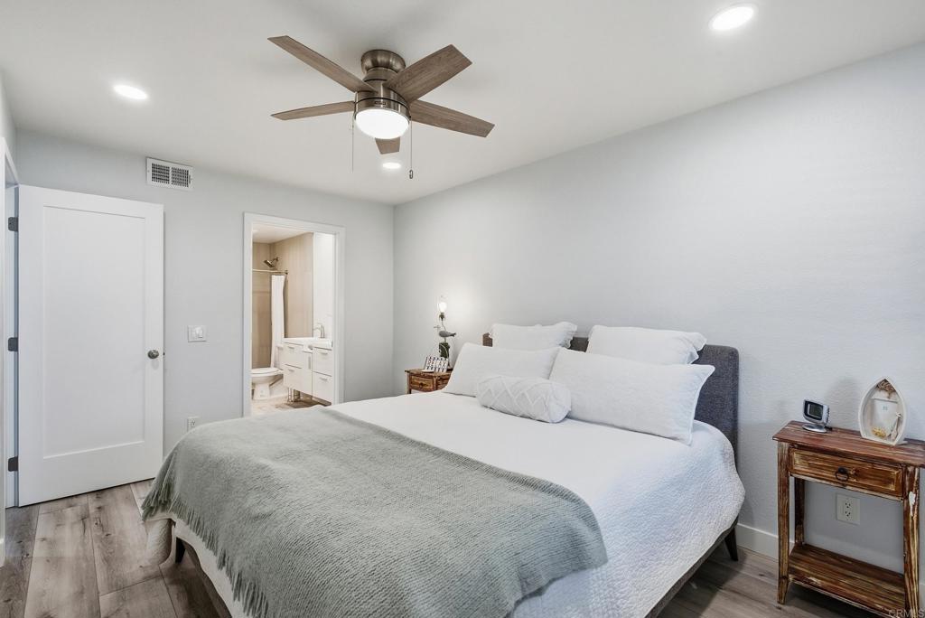 Bedroom with a large bed, gray throw, wood-blade ceiling fan, and open en suite bathroom doorway.
