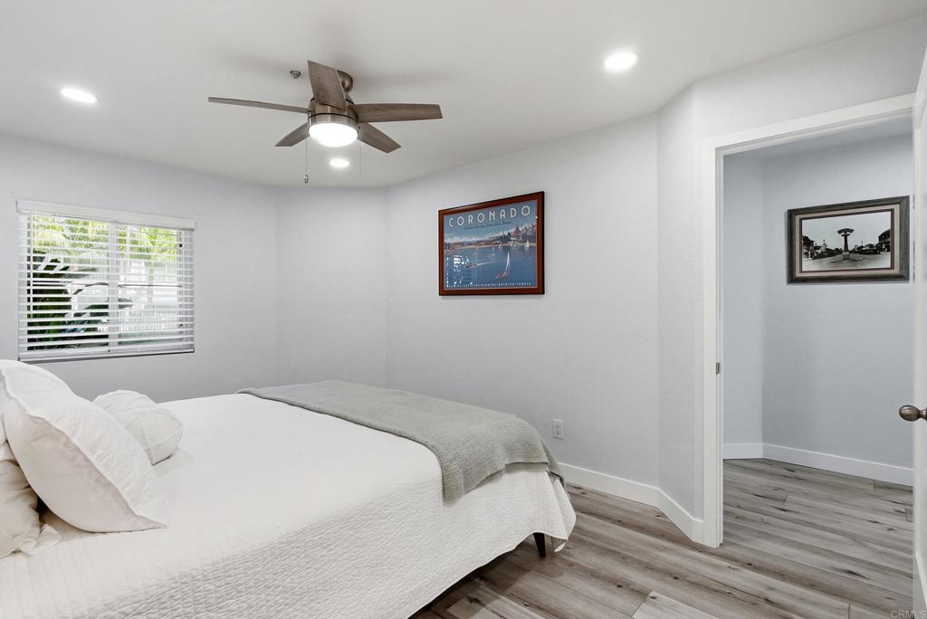 Bedroom with a white bed, gray throw, ceiling fan, and window with blinds.