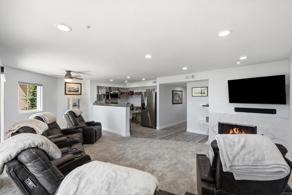 Living room with gray reclining sofas, an open kitchen, and a marble fireplace wall.