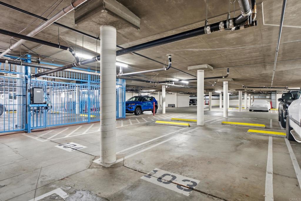 Underground parking garage with a blue security gate, marked spaces, and concrete columns.