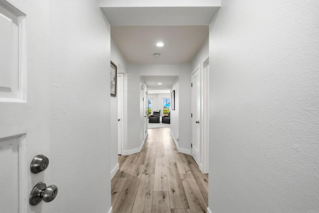 White hallway with wood-look flooring leading to a furnished living room and windows with a glimpse of water.