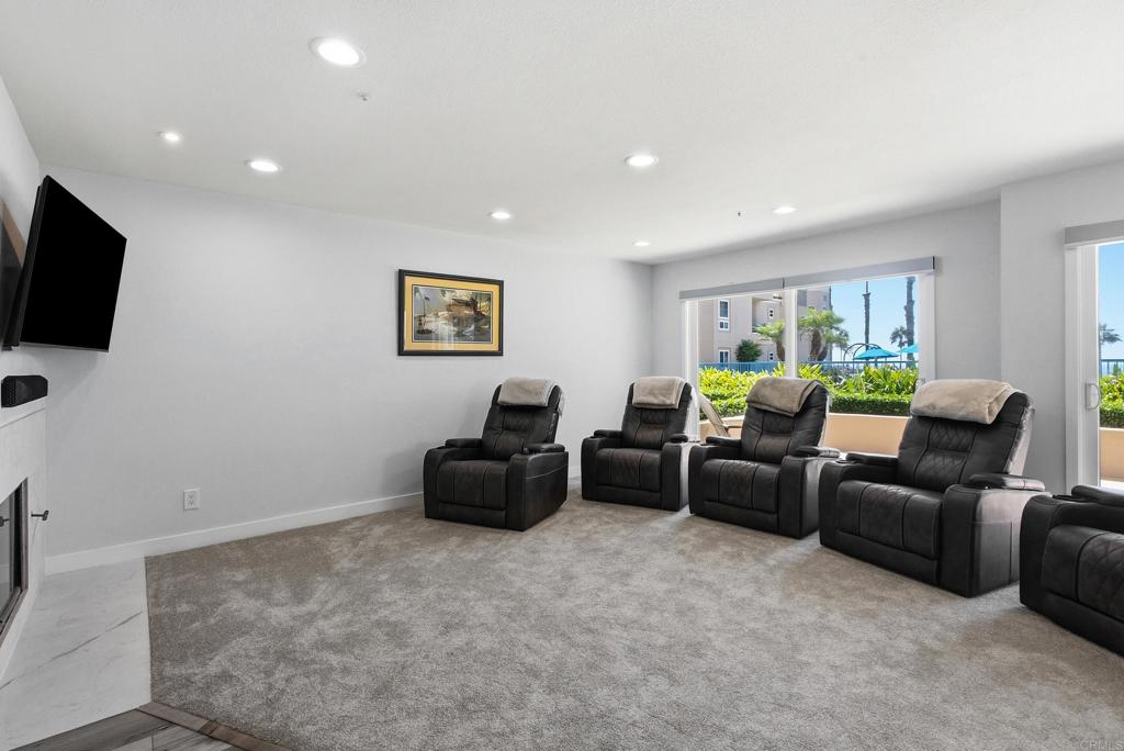 Furnished media room with black reclining chairs, a wall-mounted television, and large windows.