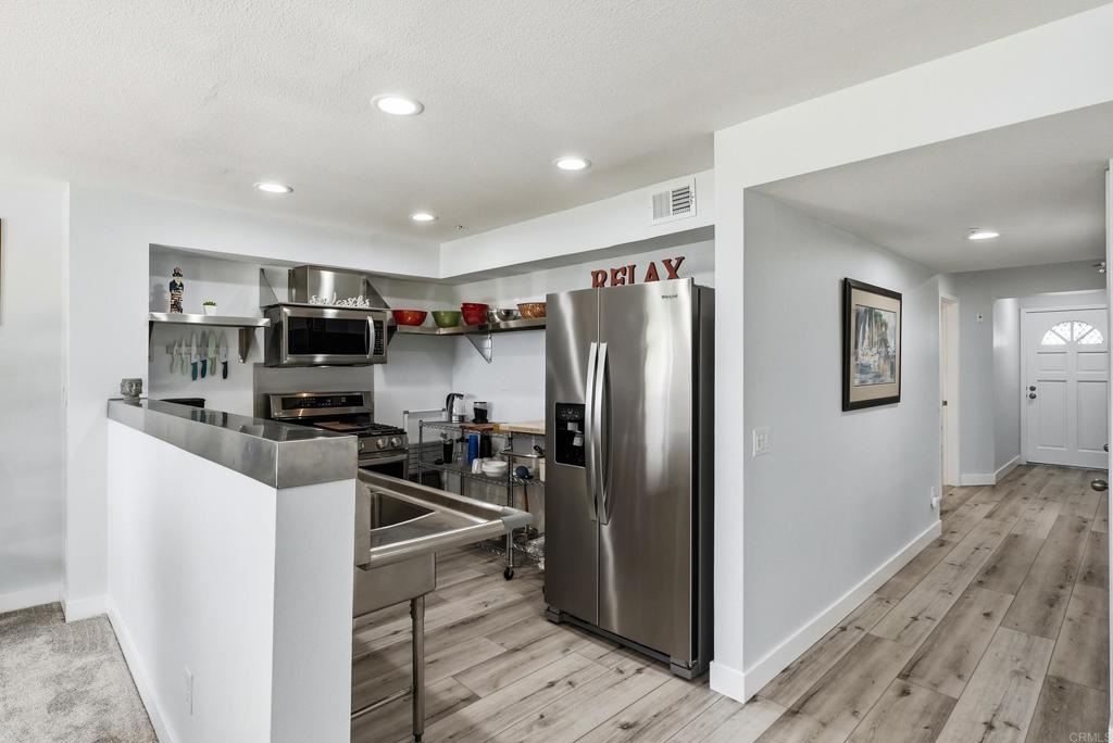 Kitchen with stainless steel appliances, a deep metal sink, open shelves, and gray wood-look flooring.