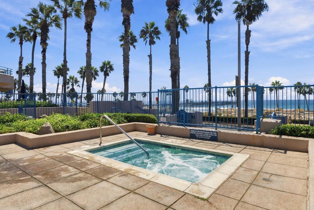 Outdoor pool terrace with palm trees and ocean views beyond a blue fence.